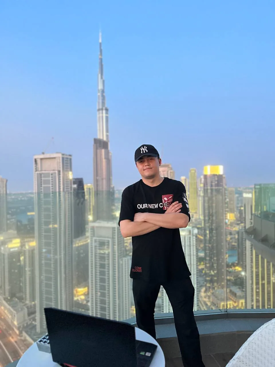 Said standing with folded arms on a balcony in Downtown Dubai, a laptop in front, the Burj Khalifa behind him